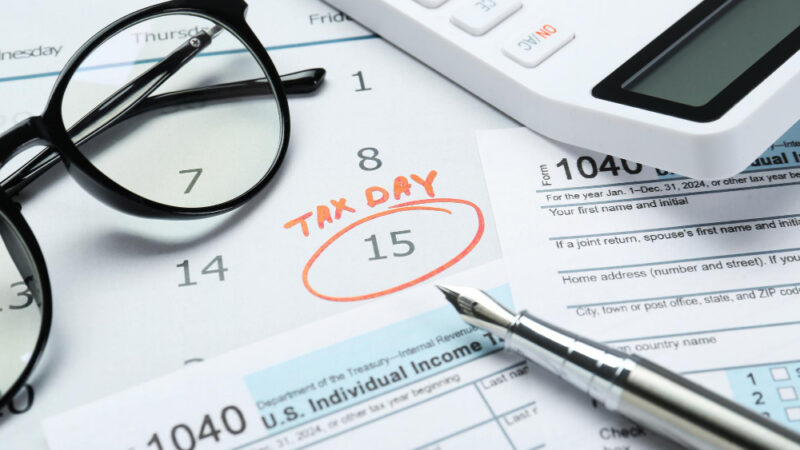 Tax day calendar with date reminder documents pen calculator and glasses on table