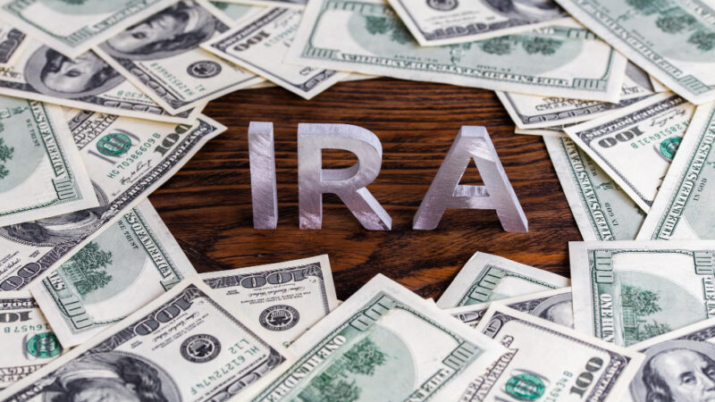 The word ira made of silver metal letters on wooden background surrounded by us dollar banknotes