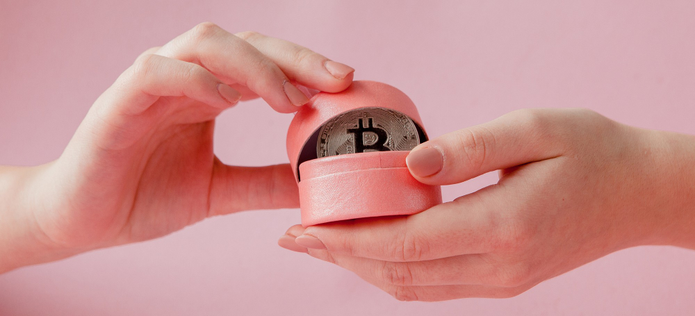 Womans hands holding bitcoin in pink gift box on a pink, symbol of virtual money.
