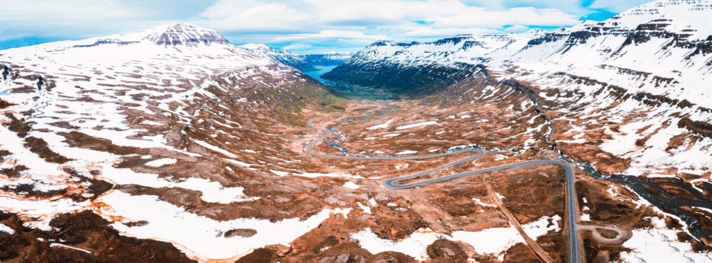 A breathtaking aerial view of a winding road through a wide valley in iceland surrounded by snowcapped mountains rocky terrain and a flowing river
