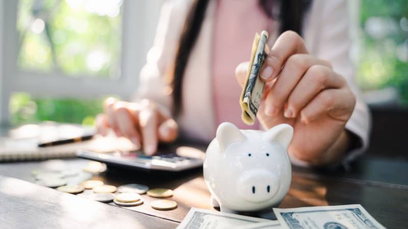Closeup of business woman hand putting money into piggy bank for saving money. Saving money and financial concept
