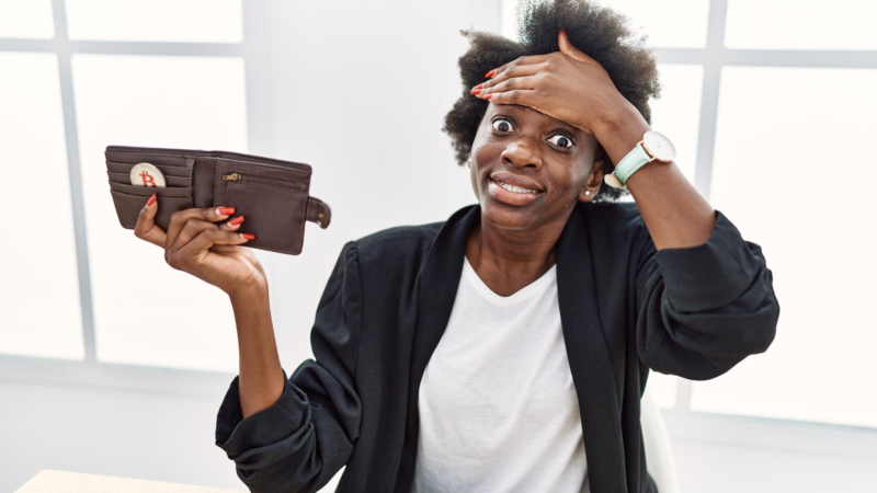 African young woman holding wallet with virtual currency bitcoin stressed and frustrated with hand on head surprised and angry face